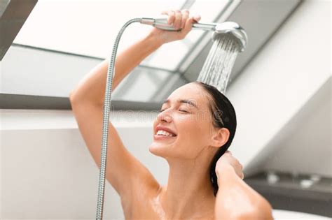 Female Washing Holding Shower Head With Running Water In Bathroom Stock