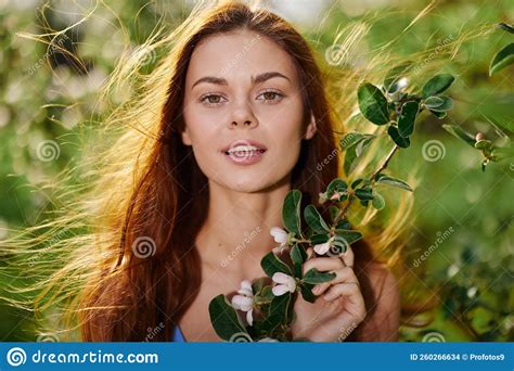 Beautiful Woman Smile Looks At The Camera Close Up With Long Red Hair Near A Tree In The Summer