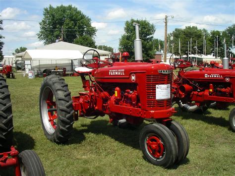 Several Red Farmall Tractors Are Parked On The Grass In Front Of Some