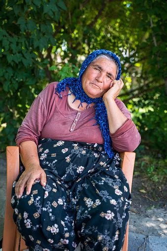 an old turkish woman wearing scarf covering head in traditional wear sitting on a chair outdoors