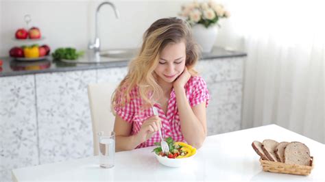 Cute Blond Girl Sitting At Table In Kitchen And Eating Salad Stock