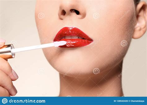 Beautiful Woman Applying Red Gloss On Lips Against Color Background