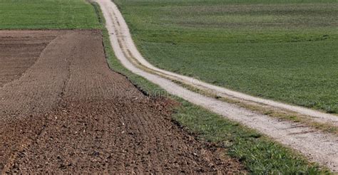 Gravel Or Country Road Through Prepared Farmland And Grass Field Stock