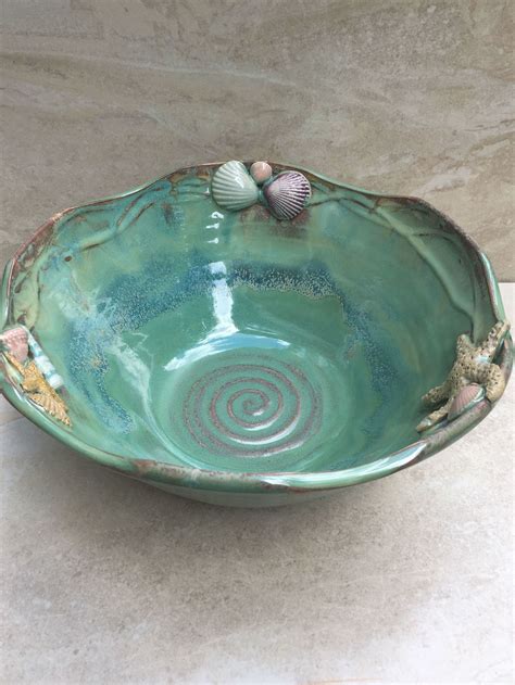 A Green Bowl With Seashells On It Sitting On A Table Next To A Marble Wall