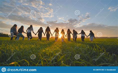 A Group Of Girls Walk Towards The Sun At Sunset Holding Hands Stock