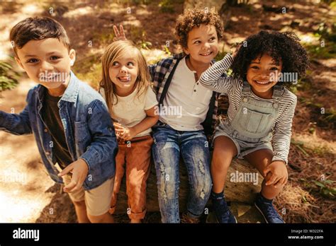 Group Of Four Kids Sitting On A Wooden Log And Having Fun Multi Ethnic