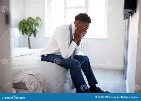 Stressed Businessman With Head In Hands Sitting On Edge Of Bed At Home