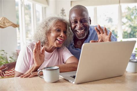 Senior Retired Couple Sitting Around Table At Home Making Video Call On