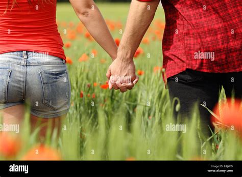 Back View Of A Romantic Couple Holding Hands In A Field With Red