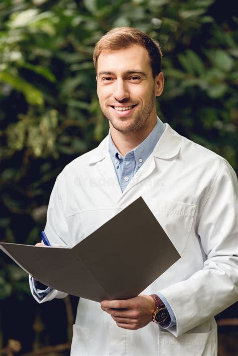 Smiling Scientist In White Coat Holding Journal In Green Orangery