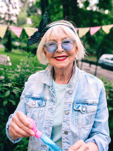 Senior Old Stylish Woman With Gray Hair And In Blue Glasses And Jeans
