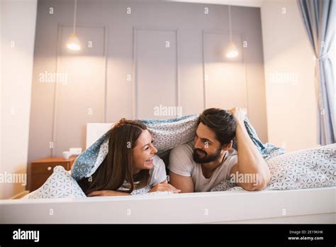 Attractive Couple Lying Under The Blanket Smiling To Each Other Stock