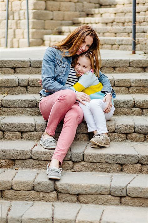 mother and daughter sitting on steps holding each other by stocksy contributor jakob