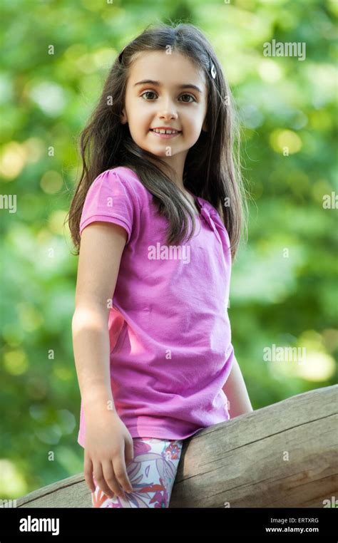 Cute Little Girl Sitting Outdoors Against Green Leaves Straddling A