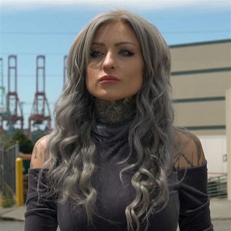 A Woman With Long Grey Hair And Tattoos On Her Neck Standing In Front
