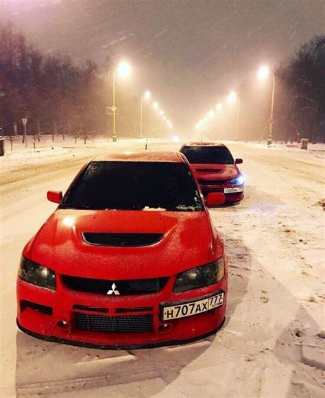 Two Red Sports Cars Parked On The Side Of A Snow Covered Road In Front Of Street Lights