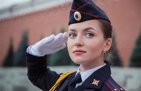 A Woman In Uniform Saluting With Her Hand On Her Head And Looking Off
