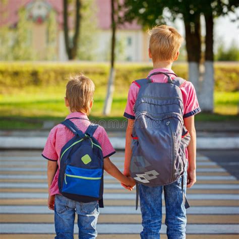 Two Kids With Backpacks Walking On The Road Holding School Time Stock