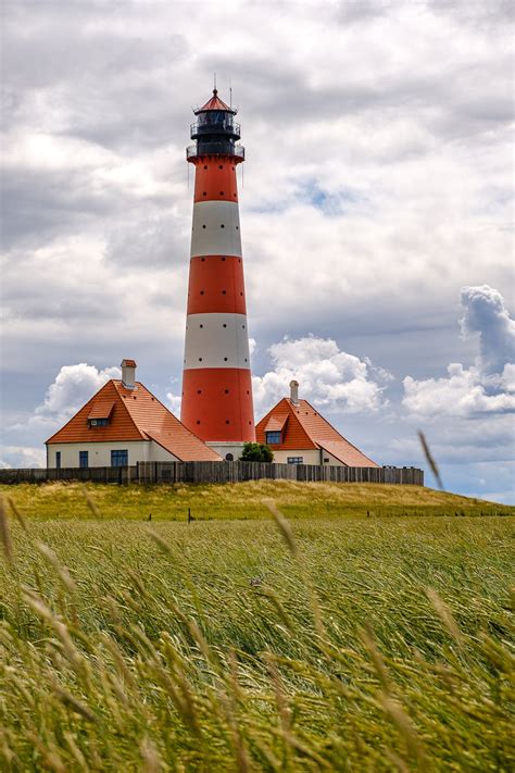 Red And White Lighthouse On Green Grass Field Under Cloudy Sky · Free