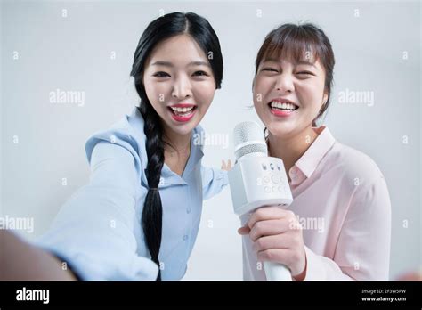 Two Asian Women Sisters Singing With Wireless Mic And Mobile Karaoke Application On Phone Stock