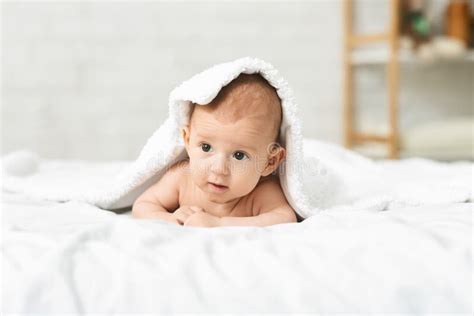 Adorable Newborn Baby Lying On Bed Under White Blanket Stock Photo