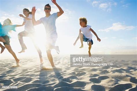 Caucasian Parents And Children Jumping For Joy On Beach High Res Stock