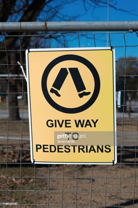 Give Way To Pedestrians Warning Sign On A Wire Mesh Fence Around A