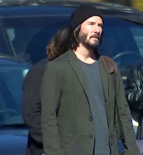 A Man With Long Hair Wearing A Black Hat And Green Jacket Is Standing