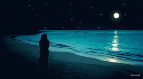 A Person Standing On Top Of A Beach Under A Full Moon At The Ocean S Edge