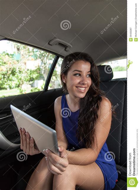 Young Woman In Back Seat Of Car With Tablet Smiling At Other Pas Stock