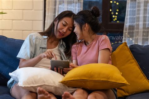 Happy Asian Lesbian Couple Using Tablet Together At Sofa In Living Room