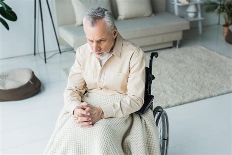 Вид сверху на грустного пенсионера инвалида сидящего в инвалидной коляске со сжатыми руками