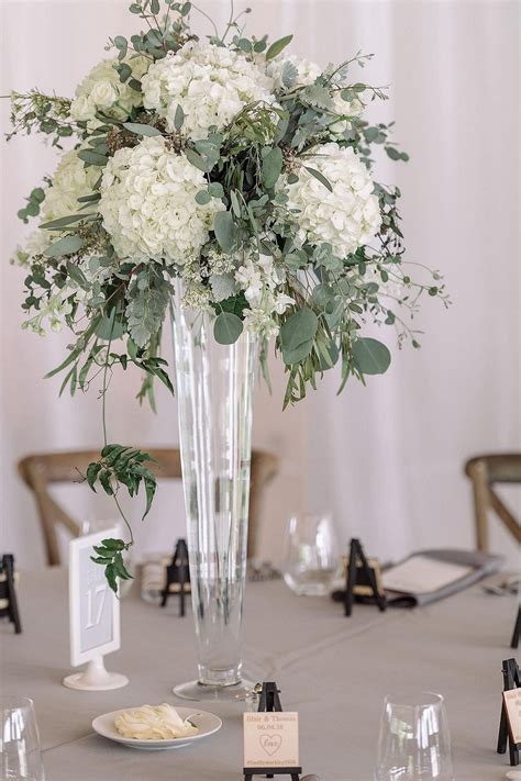 a vase filled with white flowers sitting on top of a table next to wine