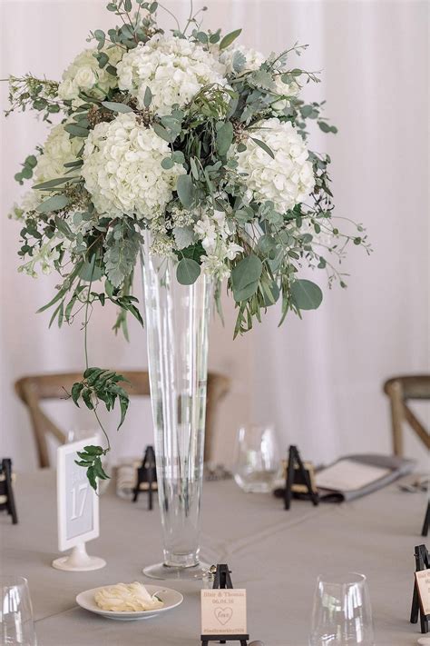 a vase filled with white flowers sitting on top of a table next to wine glasses