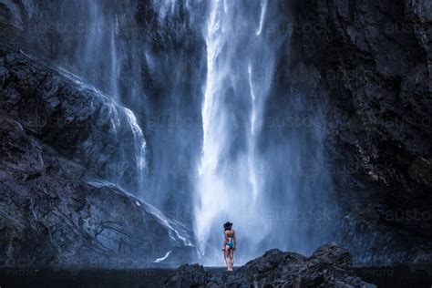 Image Of Female Standing At The Bottom Of A Giant Waterfall Austockphoto