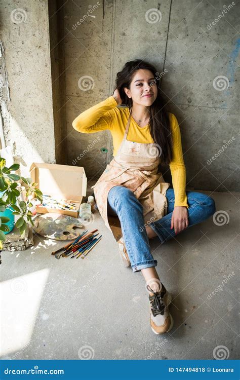 Young Beautiful Lady Artist In Apron With Paint Stains Sitting On The