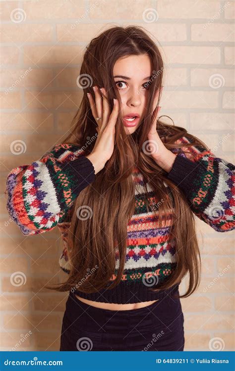 Beautiful Girl In A Multicolored Knitted Sweater Stands Near The Brick Wall Near The Window