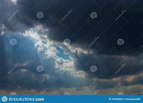 Heavenly Sun Rays Through Dark Clouds Against The Blue Sky Stock Photo