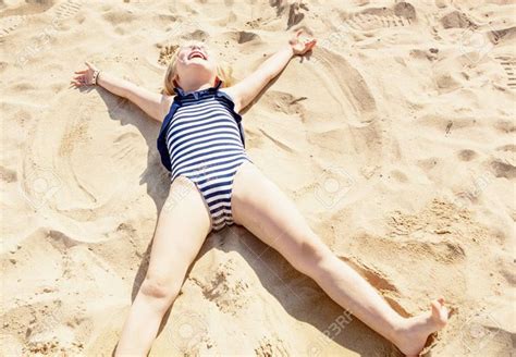 niña feliz en traje de baño poniendo en la arena y haciendo ángel en la orilla del mar fotos