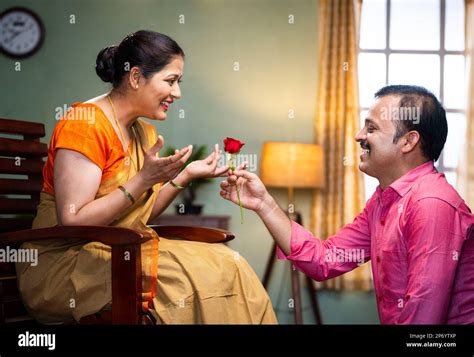 Happy Middle Aged Man Proposing His Wife By Giving Red Rose At Home