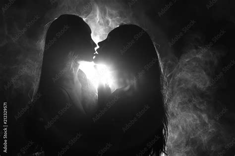 silhouette of two sexy woman kissing holding in darkness through light and smoke stock 写真