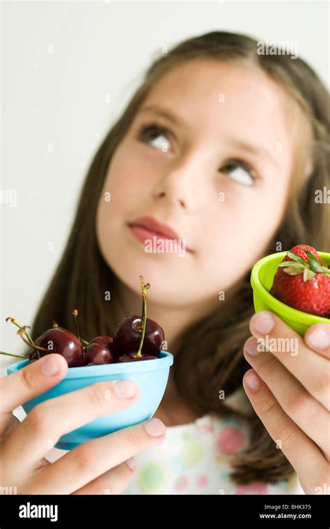 Girl Deciding Between Bowl Of Cherries And Bowl Of Strawberries Stock