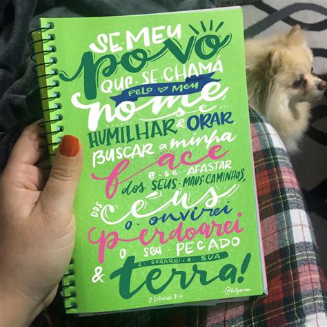 A Person Holding A Green Notebook With Writing On It And A Dog In The