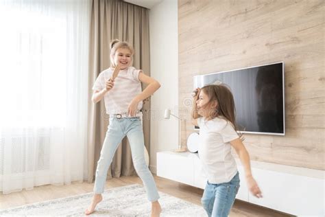 Two Sisters Having Fun Dancing In Living Room And Singing Karaoke