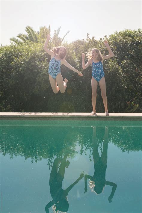 Teenage Girl Jumping Into A Swimming Pool With Her Sister Looking On Laughing By Stocksy