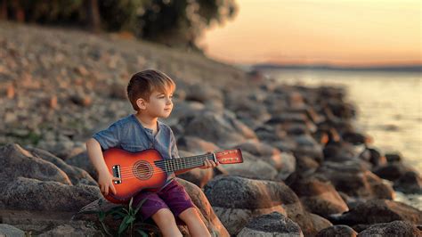 Cute Little Boy With Guitar Sitting On Rock Wearing Black Purple Dress