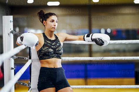 Athletic Female Boxer In Boxing Ring Leaning On Rope In The Corner