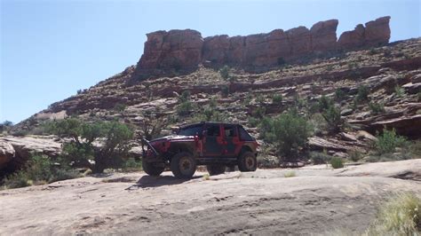 A Jeep Driving Down A Dirt Road In Front Of Some Rocks And Trees On The