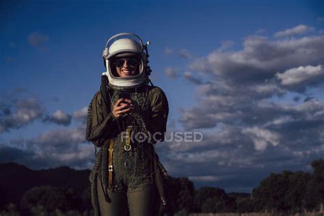 Smiling Female Astronaut In Sunglasses Holding Mobile Phone Against