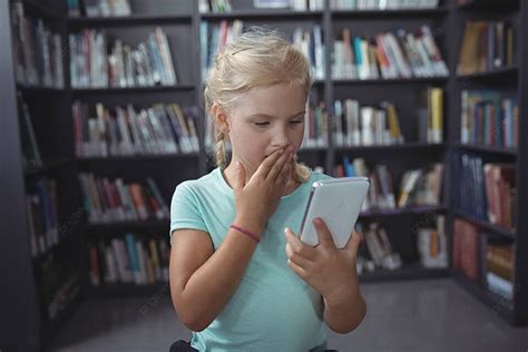فتاة متفاجئة تنظر إلى الهاتف الذكي في المكتبة صورة الخلفية والصورة للتنزيل المجاني Pngtree